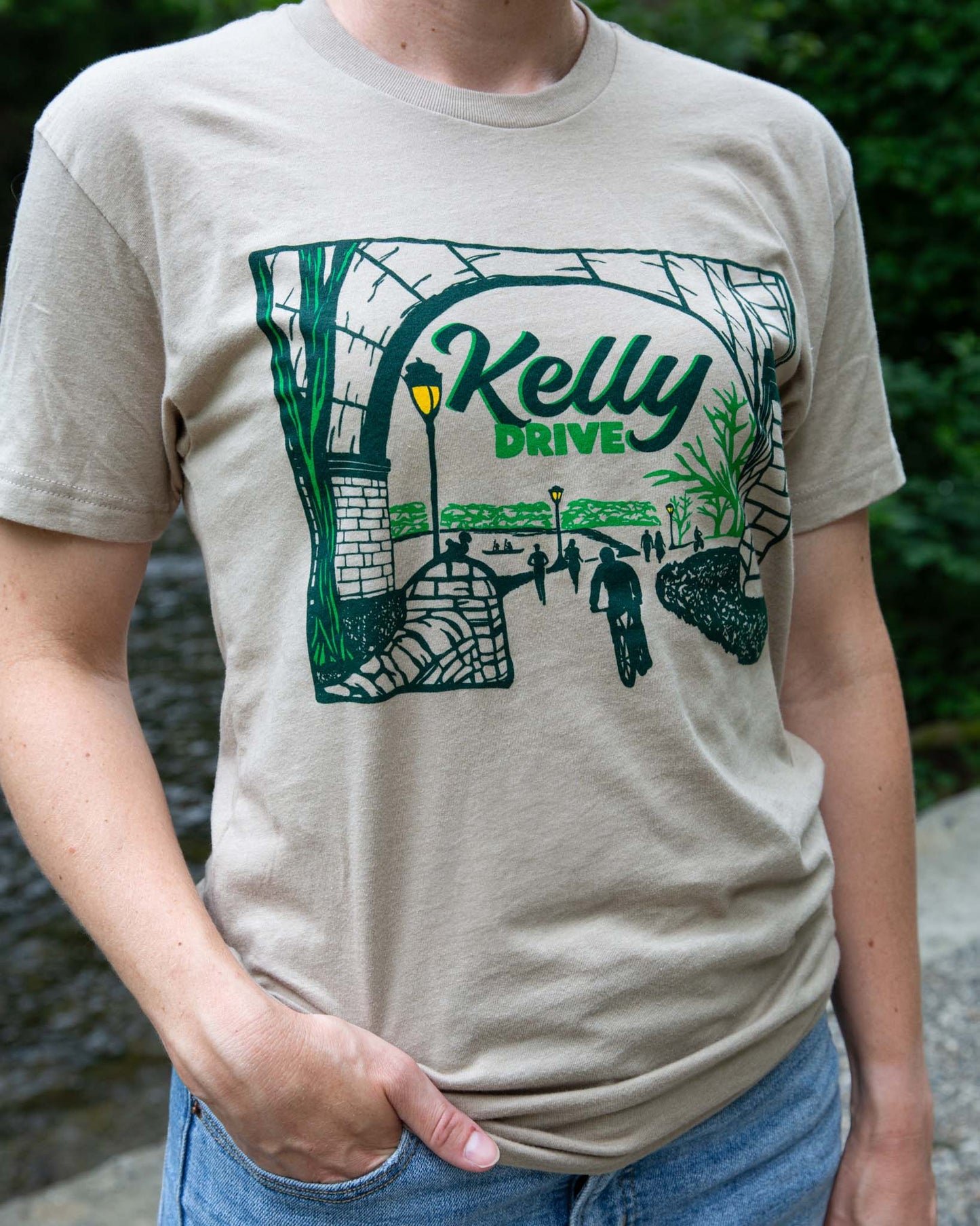 Person wearing a beige t-shirt with a green graphic design and 'Kelly Drive' text.