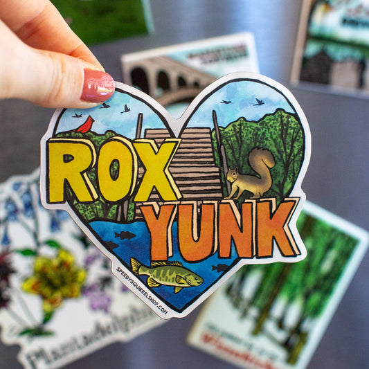 Heart-shaped sticker with 'Rox Yunk' text held by a hand in front of a fridge