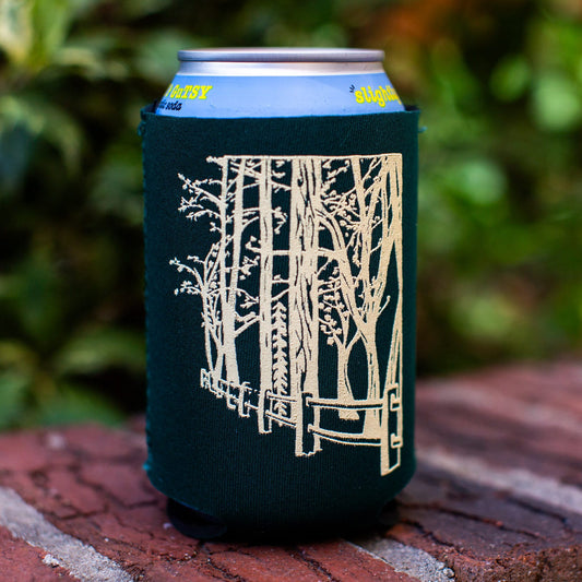 Dark green can cooler with tree design on a brick surface with blurred greenery in the background
