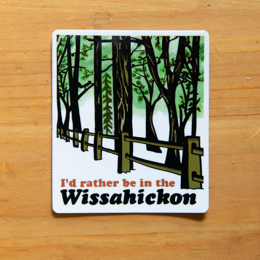 sticker with a forest design and text 'I'd rather be in the Wissahickon' on a wooden surface.