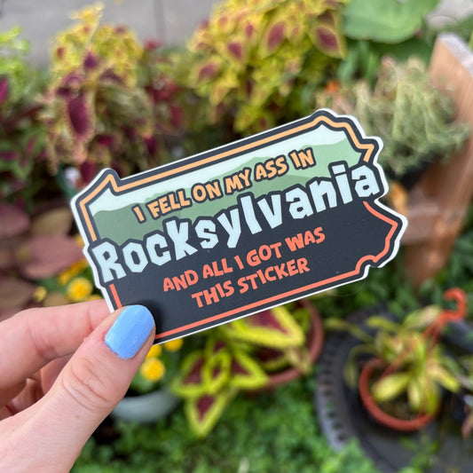 Person holding a Pennsylvania shaped sticker with text "I fell on my ass in Rocksylvania and all I got was this sticker"