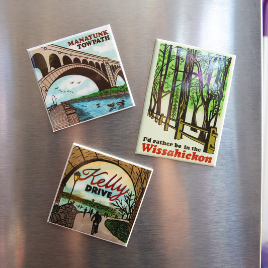 Three magnets with scenic designs on a metallic surface