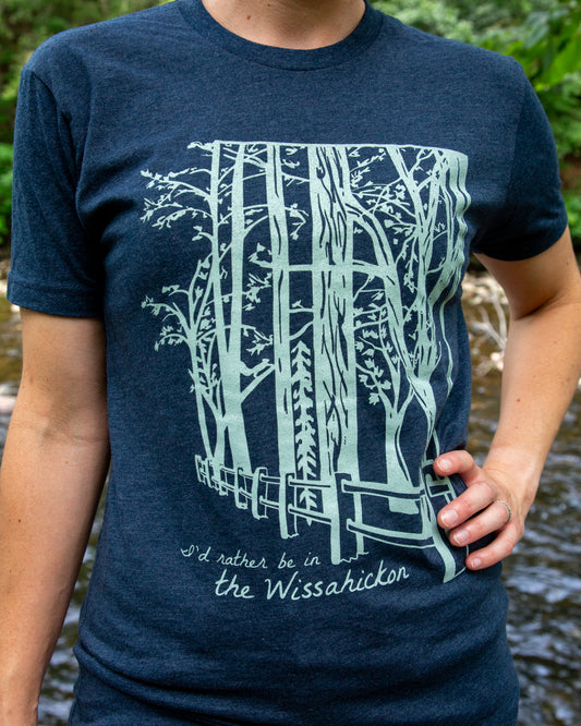 Person wearing a navy blue t-shirt with a forest design and text, standing outdoors.