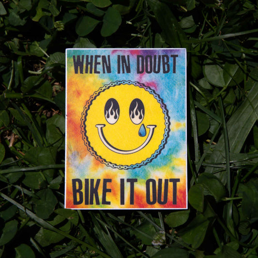 Colorful sticker with a smiley face and text 'When in doubt, bike it out' on a grass background