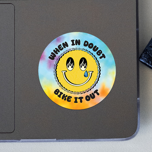 Round sticker with smiley face and text 'When in doubt, bike it out' on a laptop.