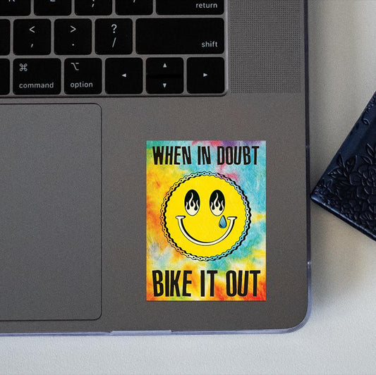 colorful sticker with a smiley face and text 'When in doubt, bike it out' on a laptop