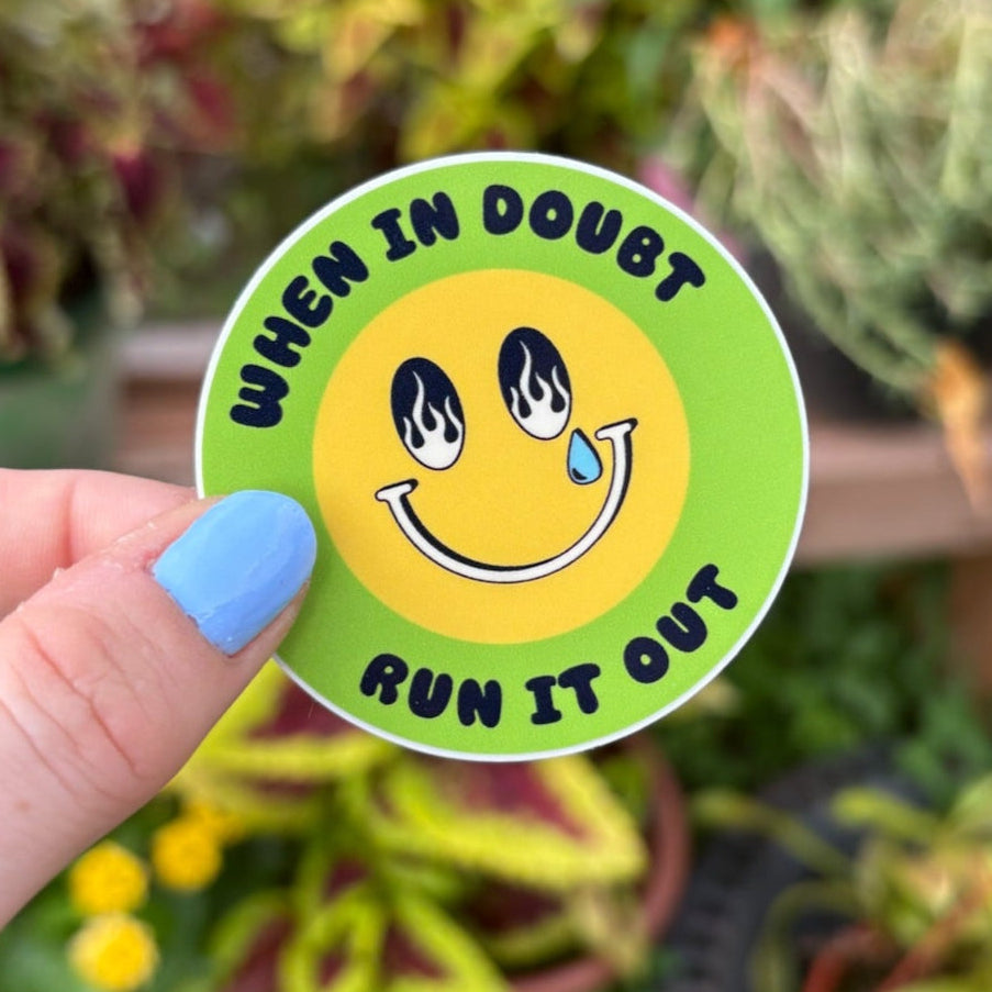 Hand holding a sticker with a smiley face and text in front of potted plants. Text says "when in double run it out."