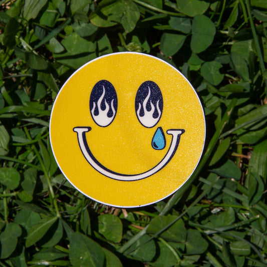 Smiley face sticker with flame eyes and a tear on grass