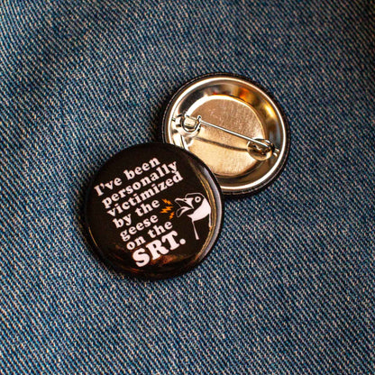 Black round pin with text 'I've been personally victimized by the geese on the SRT." with illustration of an angry Canada goose.