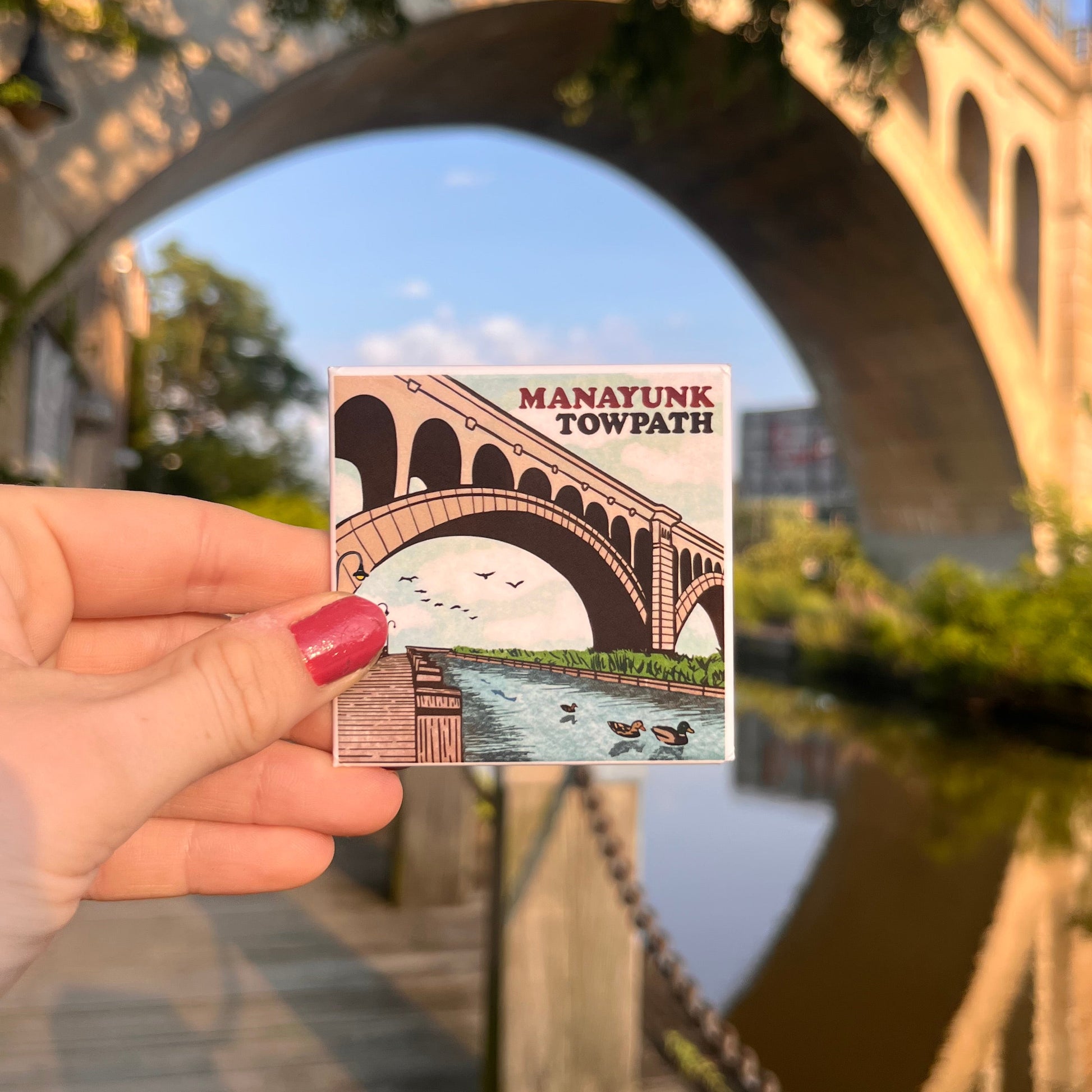 Manayunk Towpath magnet held in front of bridge on a sunny day