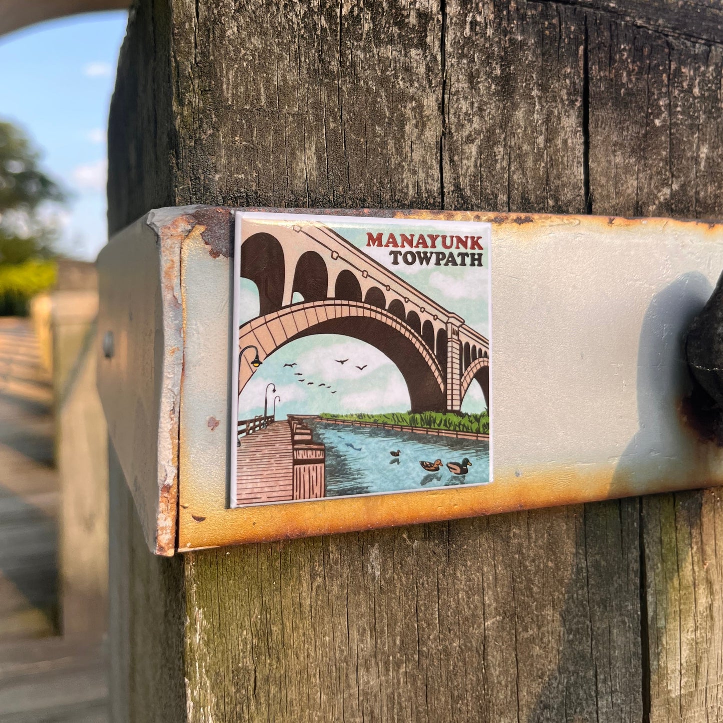 Manayunk Towpath magnet on a wooden post with trees and blue sky in the background