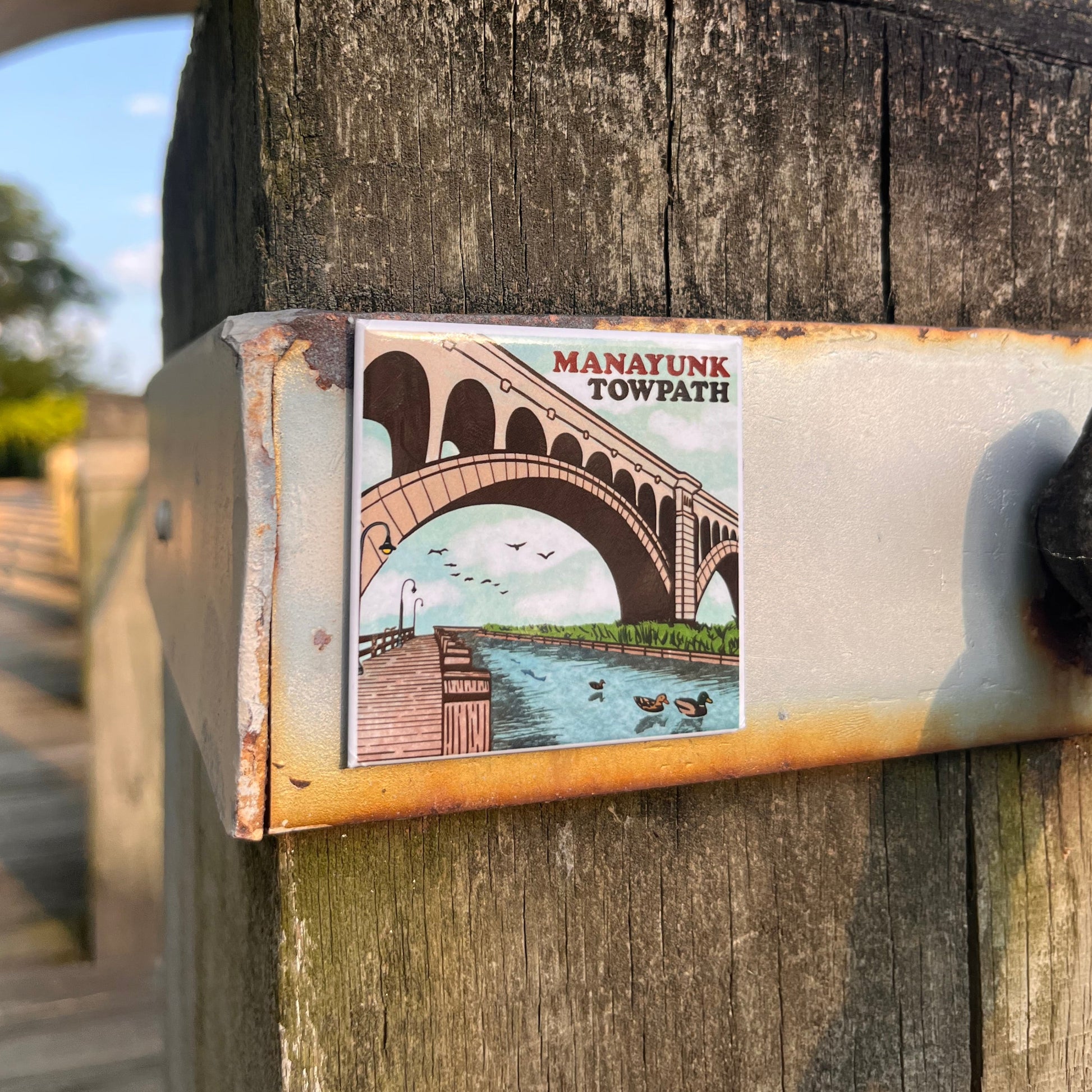 Manayunk Towpath magnet on a wooden post with trees and blue sky in the background