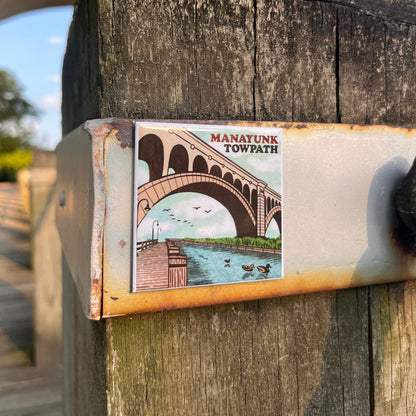 Manayunk Towpath magnet on a wooden post with trees and blue sky in the background