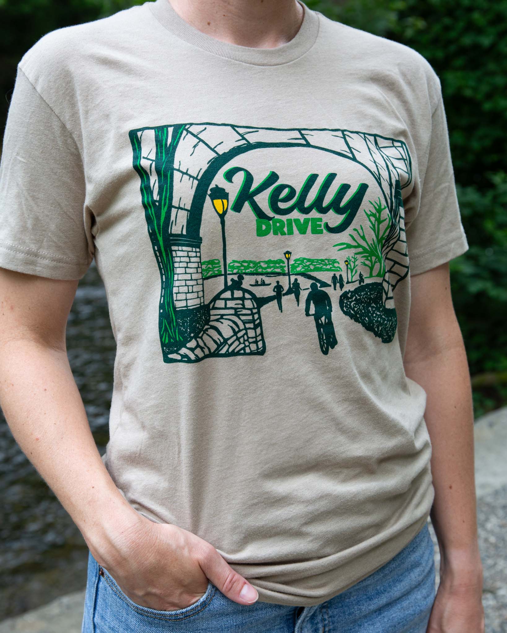 Person wearing a beige t-shirt with a green graphic design and 'Kelly Drive' text.