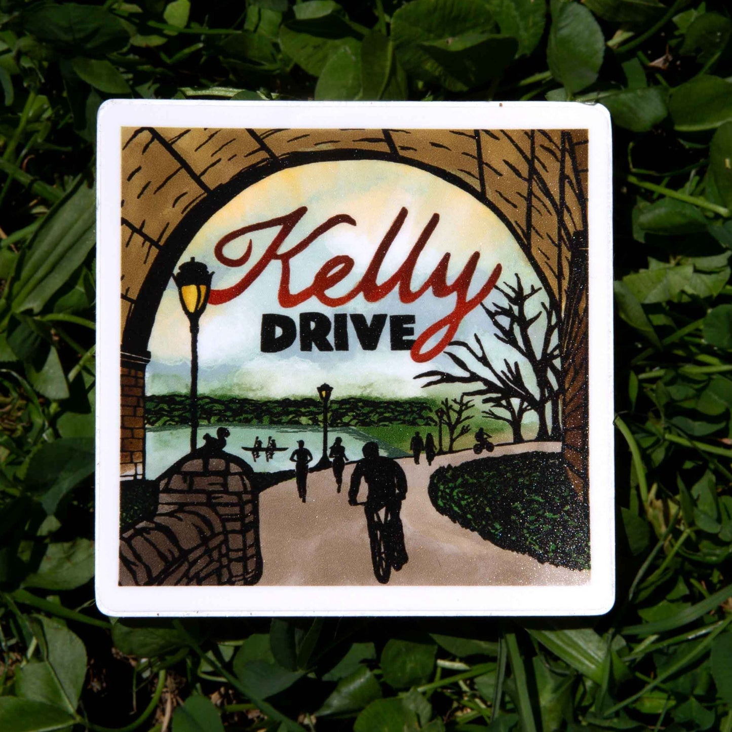 Sticker with 'Kelly Drive' text and illustrative bridge and trail design on a grass background. 