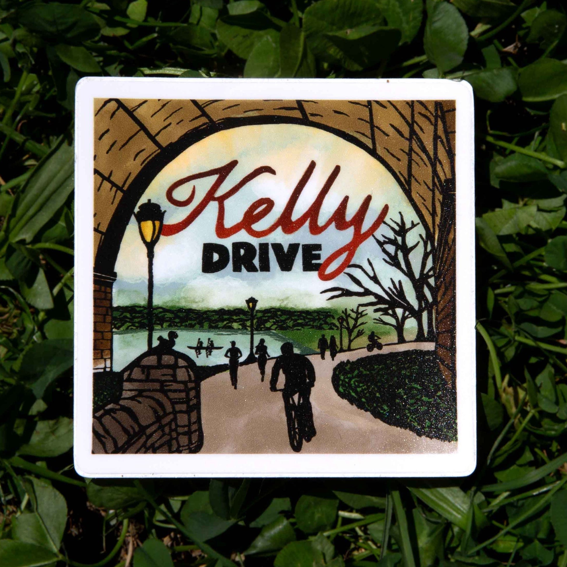 Sticker with 'Kelly Drive' text and illustrative bridge and trail design on a grass background. 