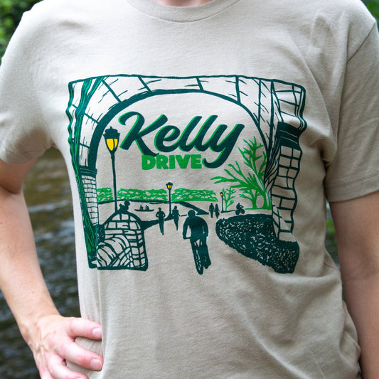 Beige t-shirt with 'Kelly Drive' design featuring a scenic view or bikers, runners and rowers on a trail.
