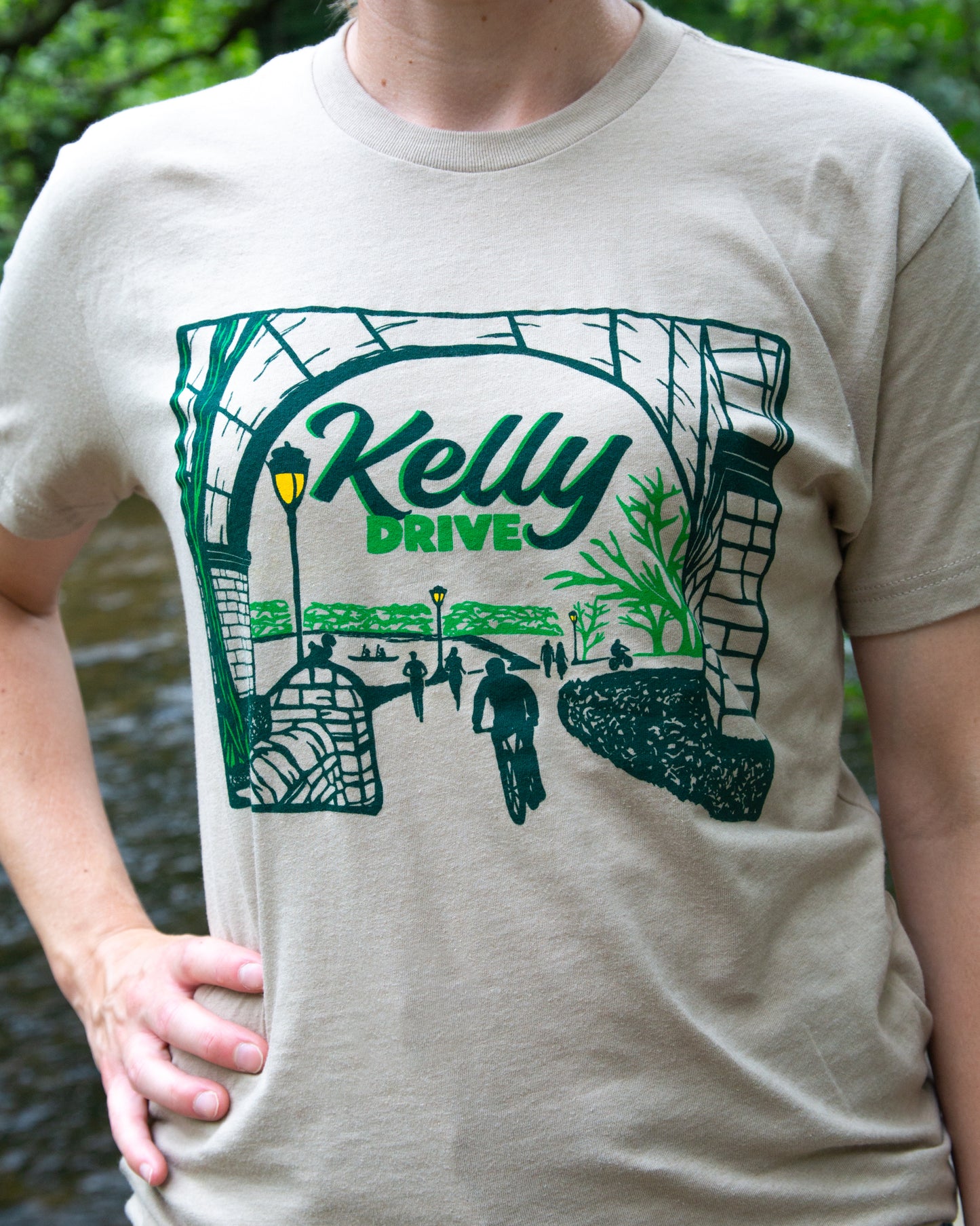 Beige t-shirt with 'Kelly Drive' graphic design featuring green text and black illustrations.