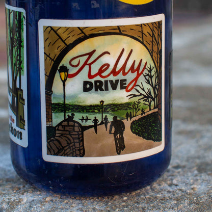 Bottle with a 'Kelly Drive' illustration sticker on a concrete surface. 