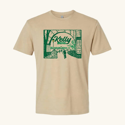 Beige t-shirt with 'Kelly Drive' design featuring a scenic view or bikers, runners and rowers on a trail, on a light blue background. 