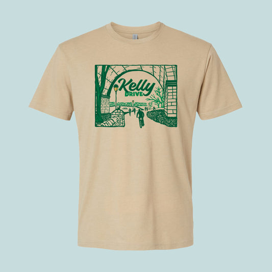 Beige t-shirt with 'Kelly Drive' design featuring a scenic view or bikers, runners and rowers on a trail, on a light blue background. 