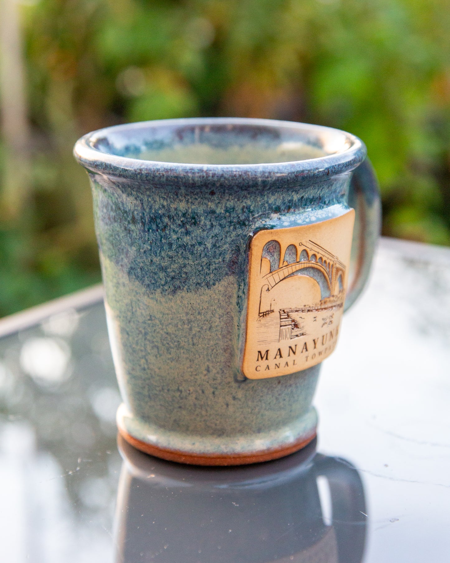 Blue ceramic mug with a leather label on a reflective surface with a blurred green background
