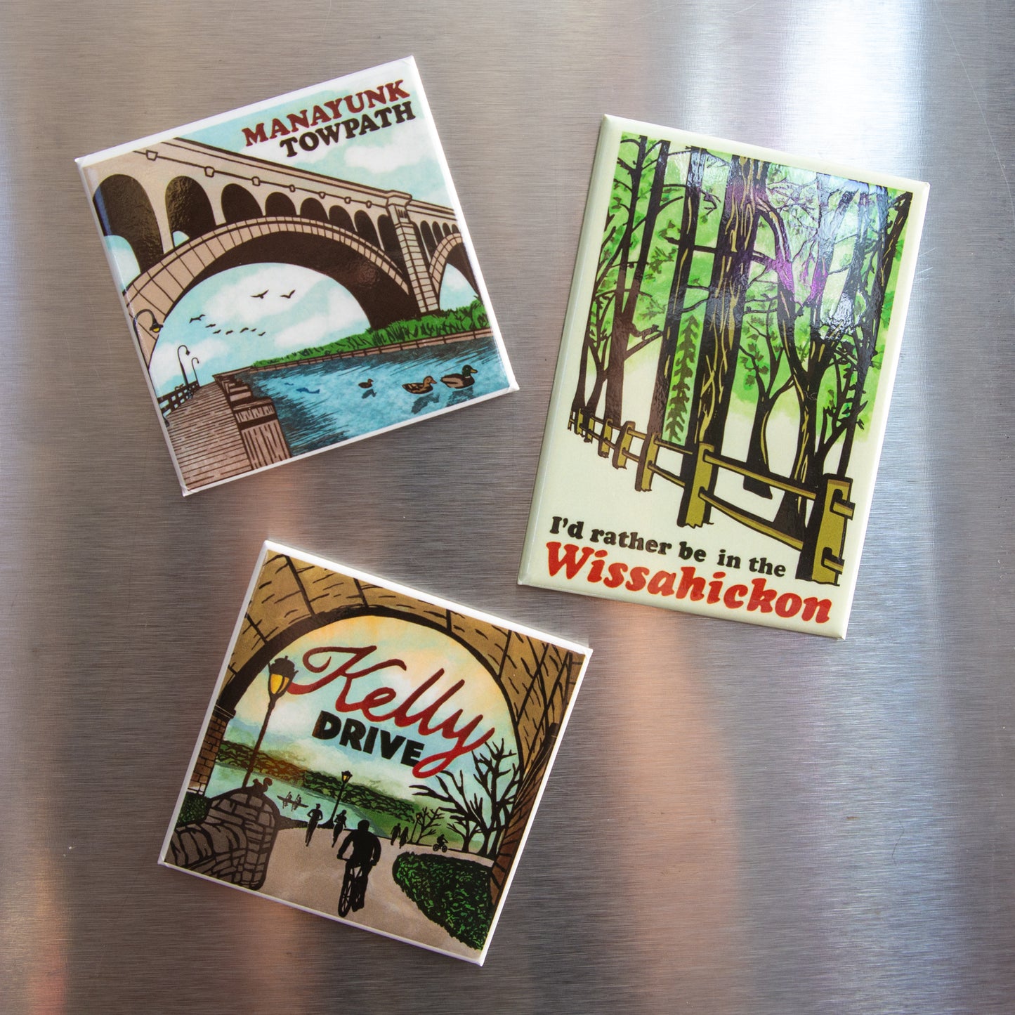 Three magnets with scenic designs on a metallic surface
