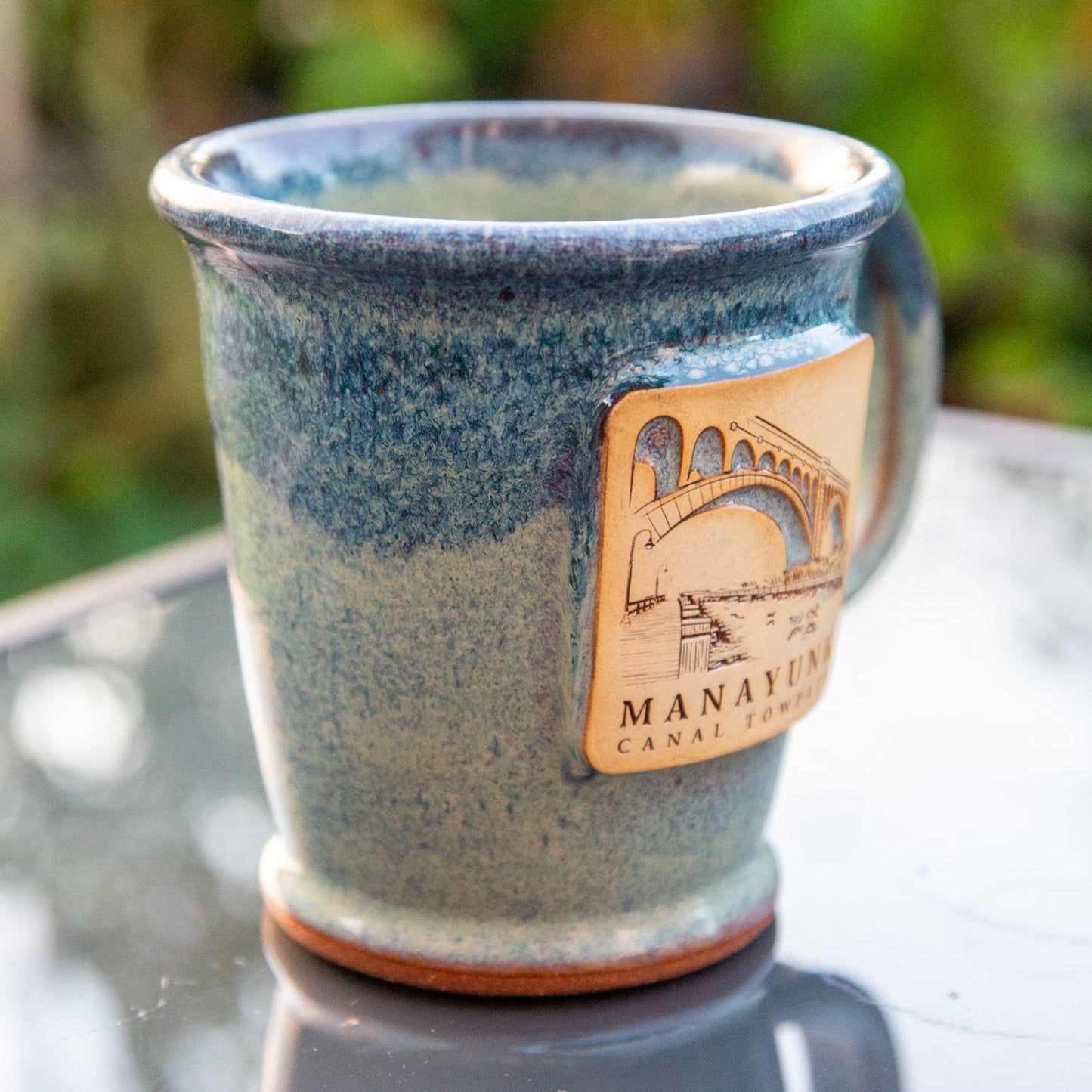 Blue ceramic mug featuring 'Manayunk Canal Towpath' on a reflective surface.