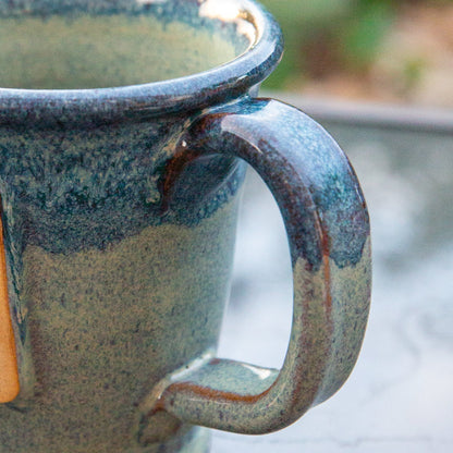 Close up of handle of handmade ceramic mug with blue gradient glaze. 