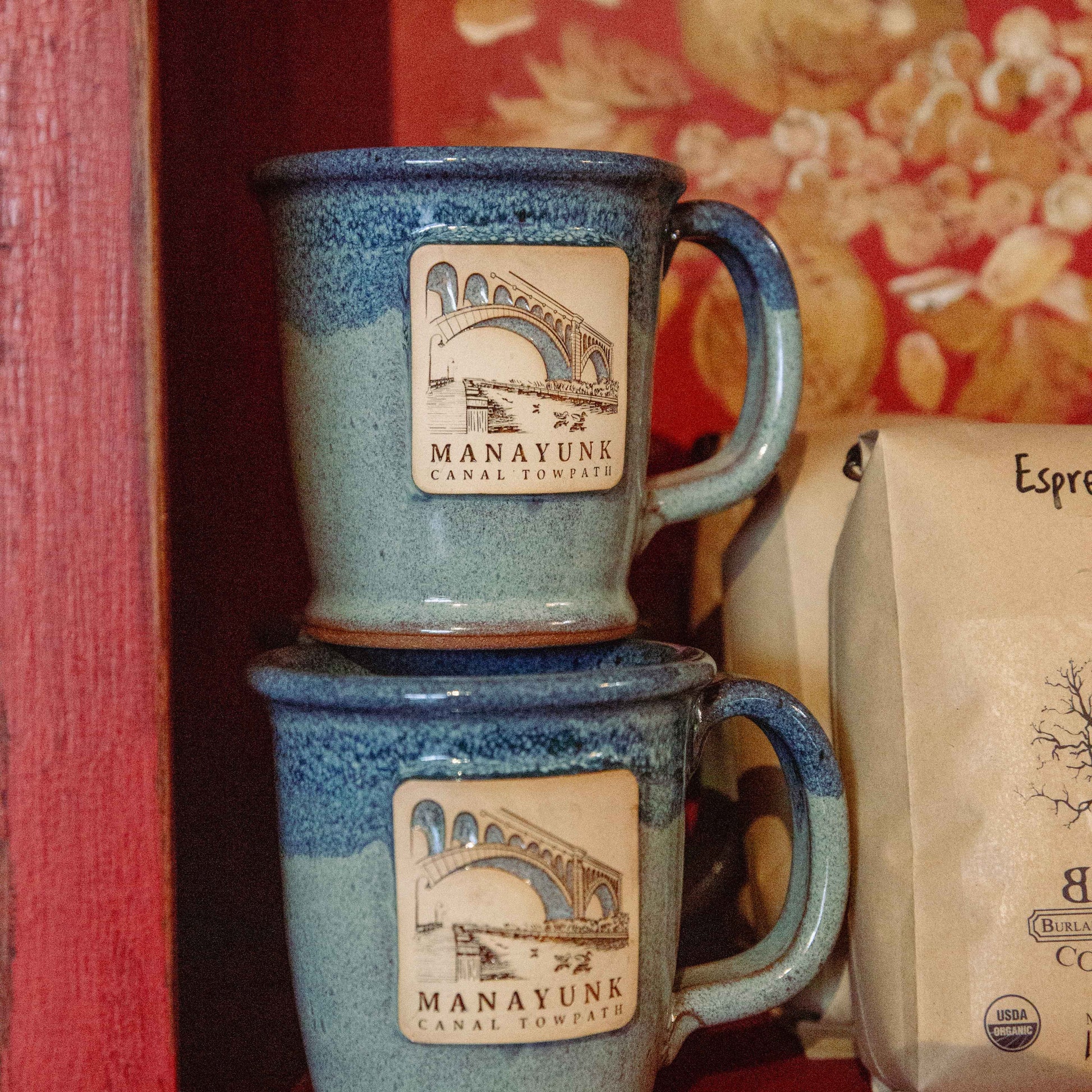 Two blue ceramic mugs with 'Manayunk Canal Towpath' clay illustration.