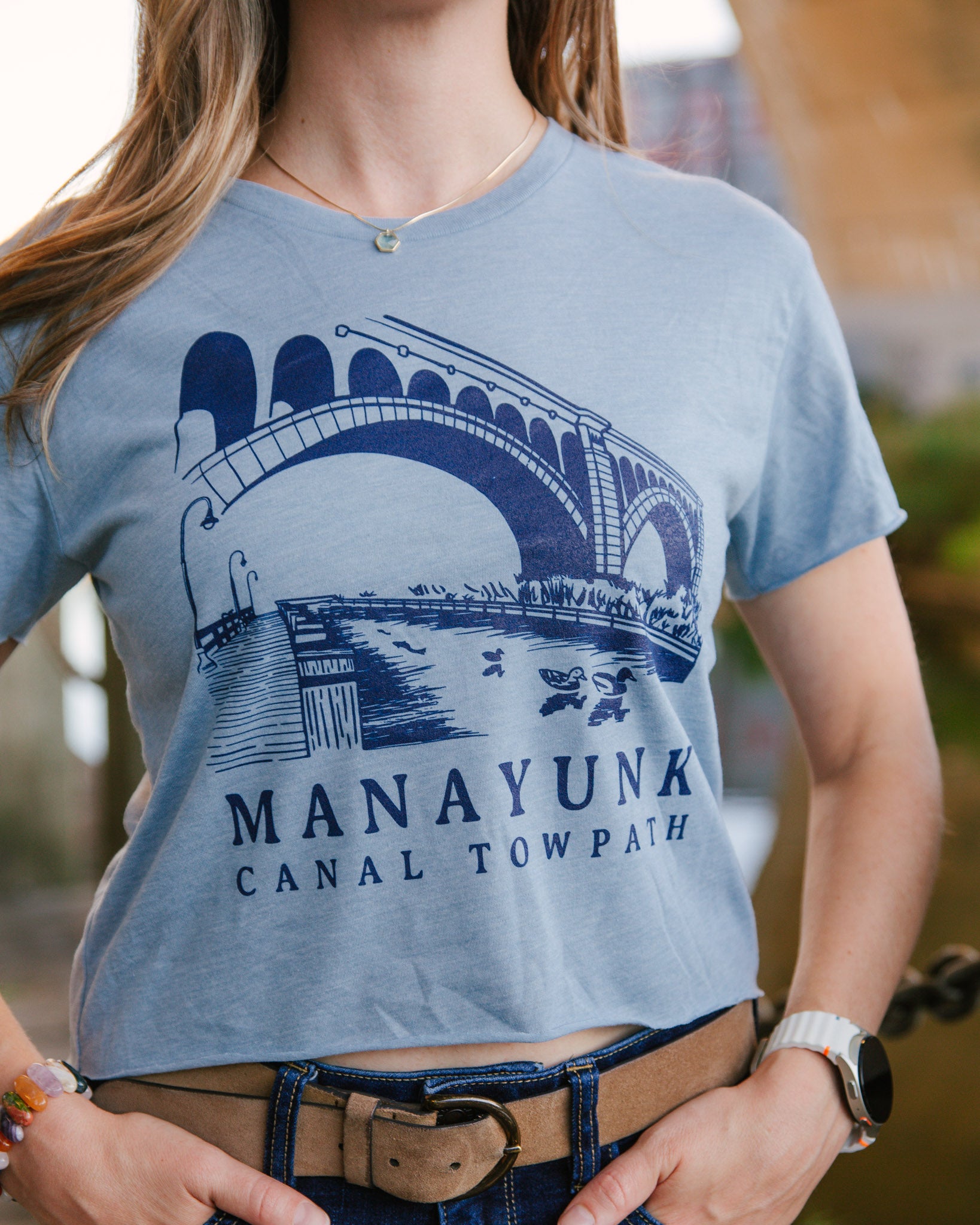 Person wearing a light blue t-shirt with a bridge graphic and 'Manayunk Canal Tow Path' text.
