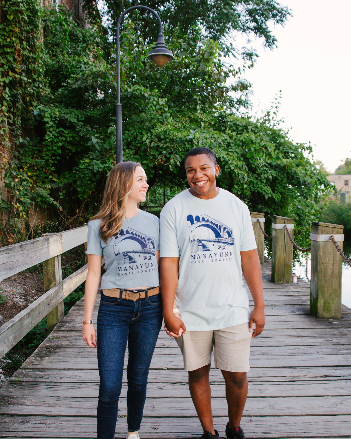 Two people standing on a wooden dock wearing matching t-shirts with a logo and text.