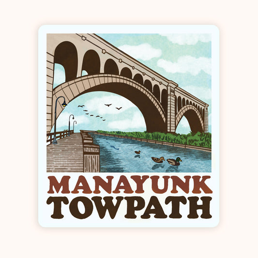 A sticker featuring an illustration of the Manayunk Towpath with a bridge, water, and birds in a stylized representation of the area. 