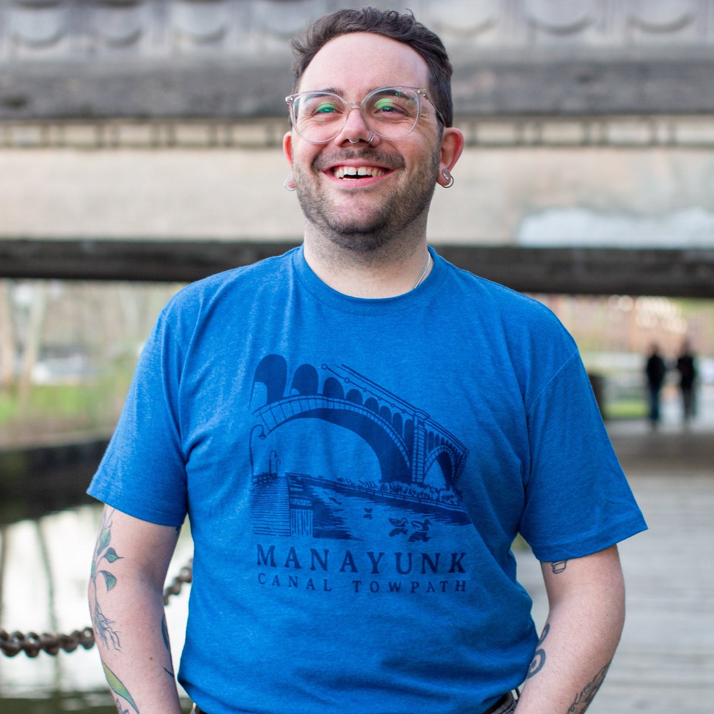 Person wearing a dark blue t-shirt with 'Manayunk Canal Towpath' design, standing outside. 