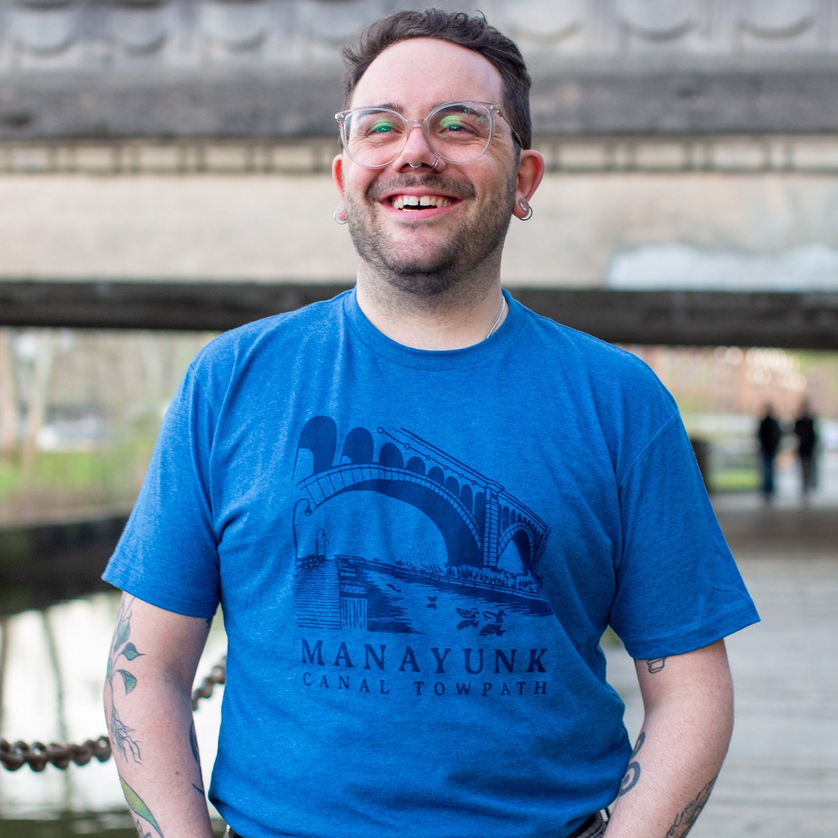 Person wearing a dark blue t-shirt with 'Manayunk Canal Towpath' design, standing outside. 