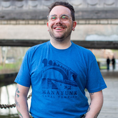 Person wearing a dark blue t-shirt with 'Manayunk Canal Towpath' design, standing outside. 