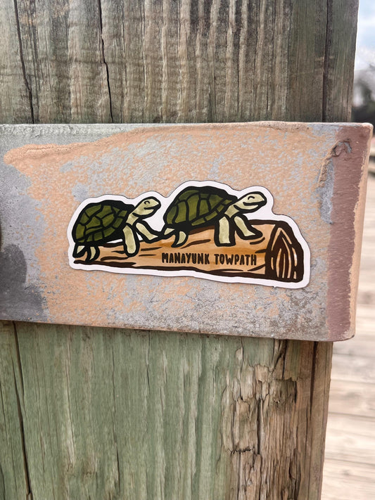  two turtles resting on a log with "Manayunk Towpath" magnatized to a fence.