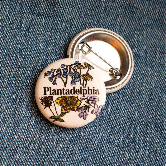Pin with 'Plantadelphia' text and floral designs on a denim background