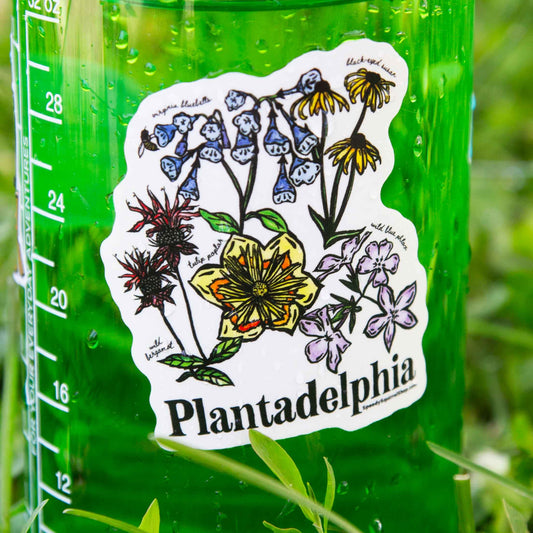 Green water bottle with a floral sticker labeled 'Plantadelphia' on grass.