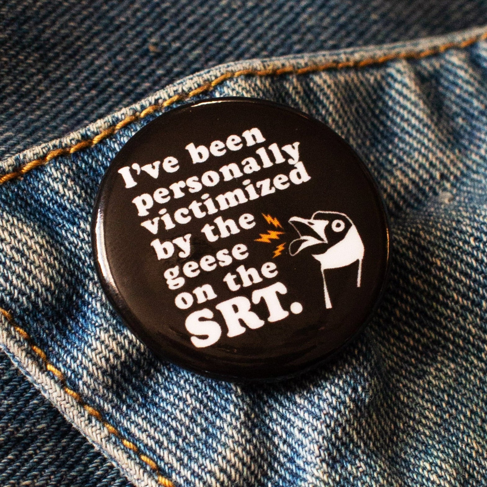 Black round pin with text 'I've been personally victimized by the geese on the SRT." with illustration of an angry Canada goose.