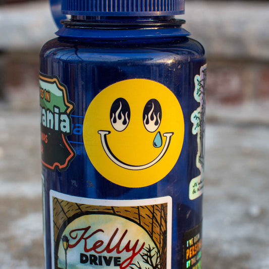 Blue bottle with stickers, including a smiley face sticker with flame eyes and a single tear.