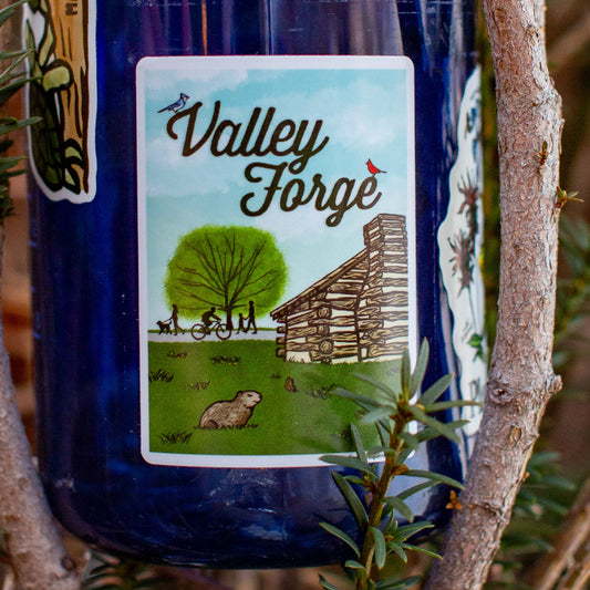Blue water bottle with a Valley Forge sticker Illustration of a log cabin, tree, and people on a bike and footpath.