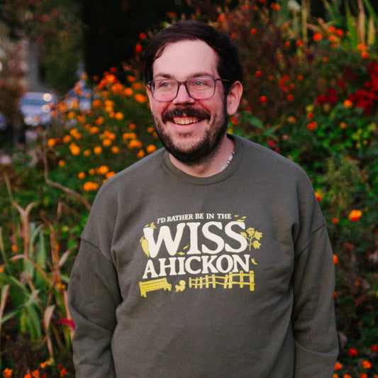 Man wearing an olive green crewneck with 'I'd Rather Be In The Wissahickon' text and graphics.