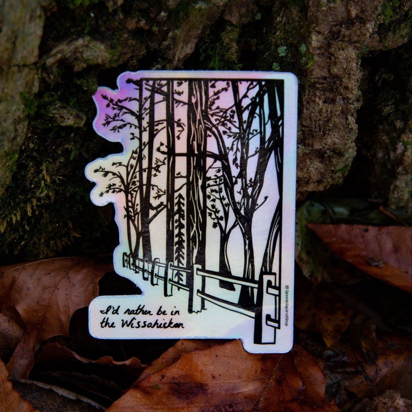 A holographic sticker with an illustration of the Wissahickon Valley Park, featuring trees and a pathway, held against a natural background with foliage.