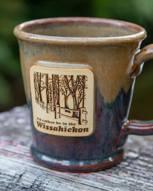 Ceramic mug with a wooden label reading 'I'd rather be in the Wissahickon' on a wooden surface.
